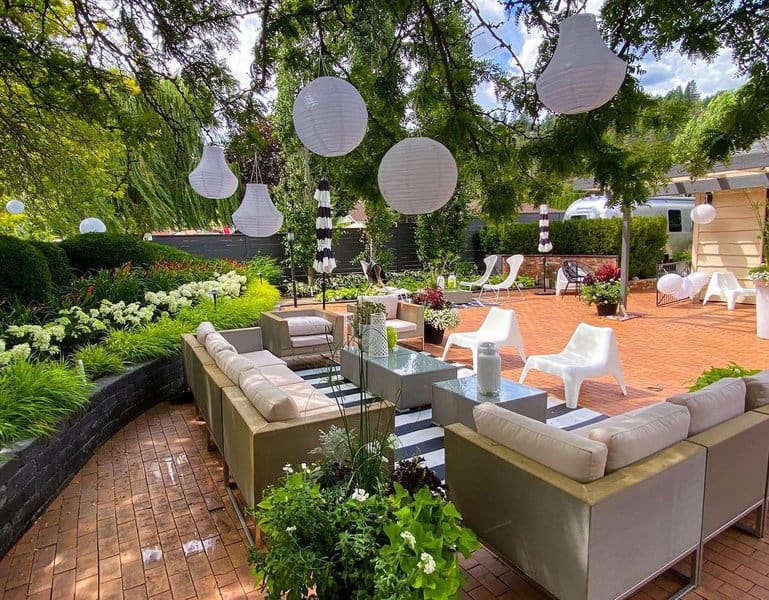 Modern patio with white sofas, hanging lanterns, and lush greenery