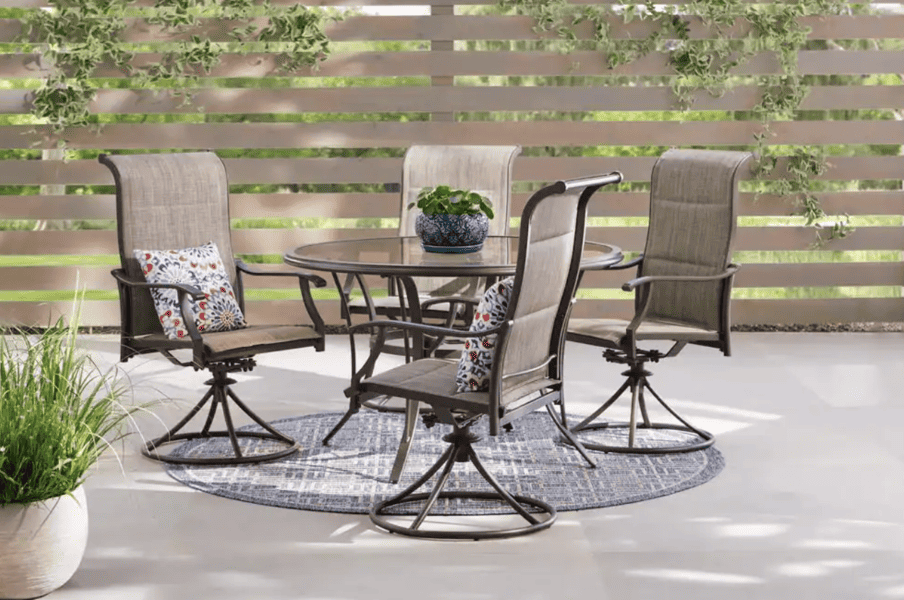 Outdoor dining set with swivel chairs, a round glass table, and decorative pillows on a patio.