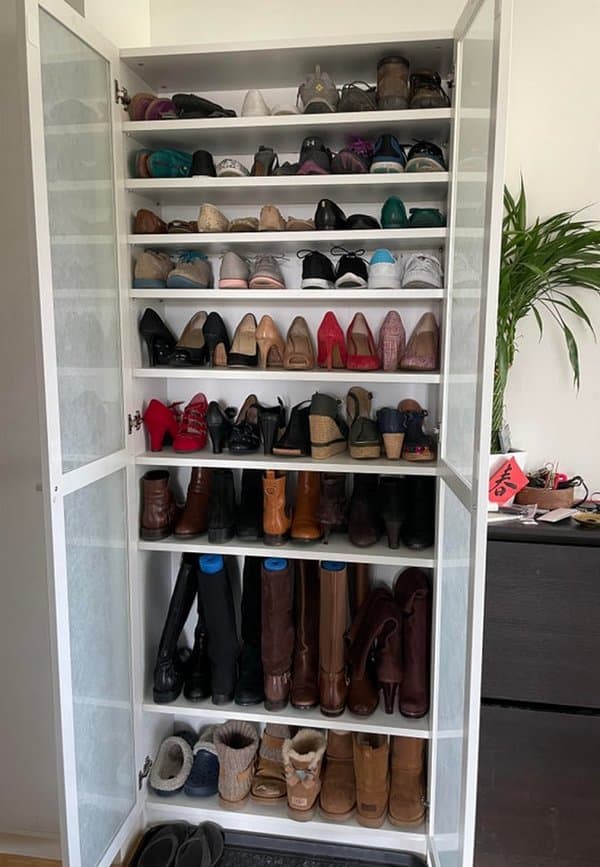 Hoher weißer Schuhschrank mit Glastüren, die verschiedene Arten von Schuhen und Stiefeln in mehreren Regalen in einem ordentlichen Layout organisieren